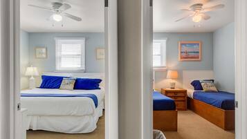 A bedroom with a bed, bedside tables, a lamp, a ceiling fan, and a window with blinds.