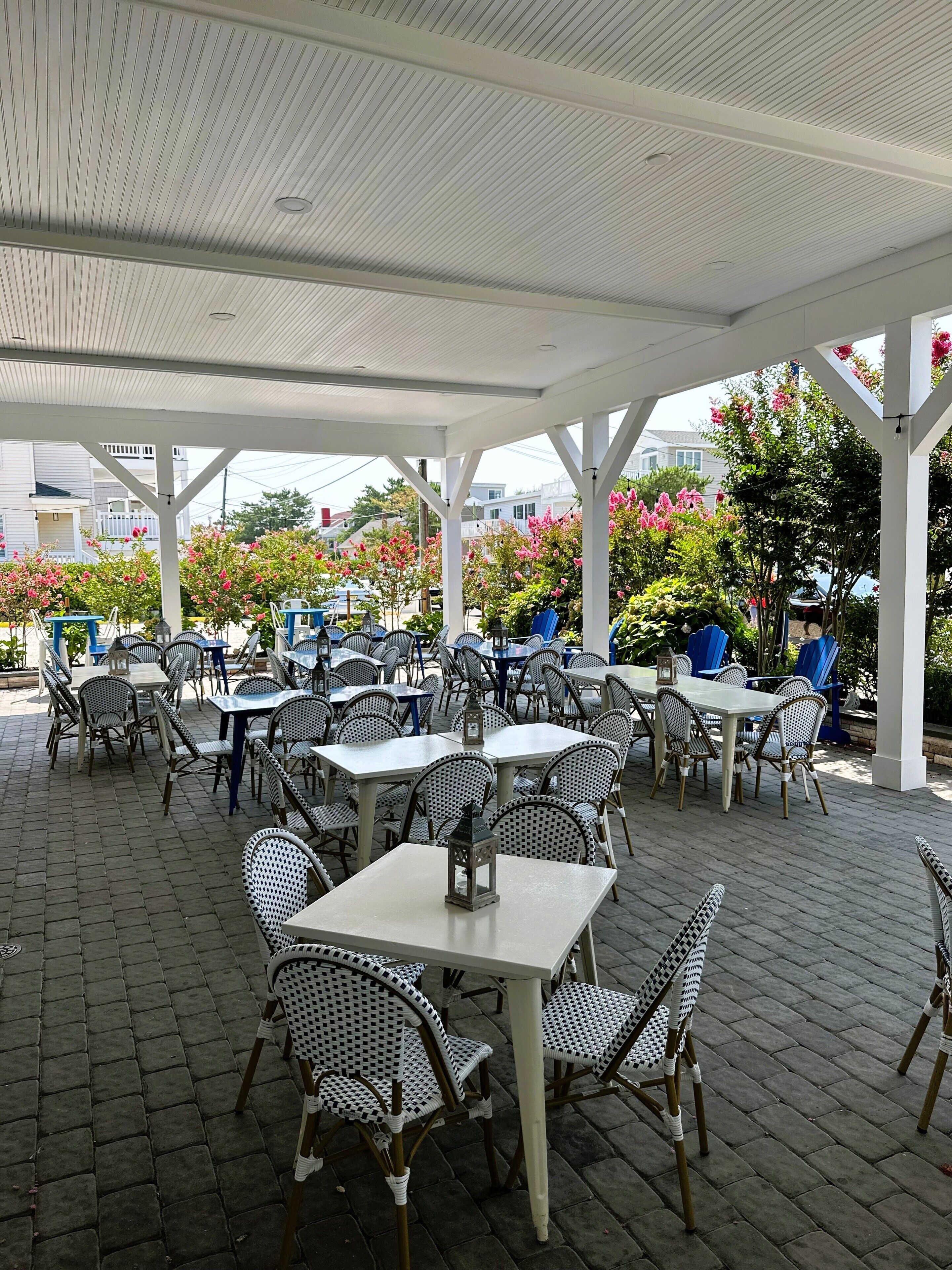 An outdoor patio with tables and chairs, a covered area, and surrounding greenery.