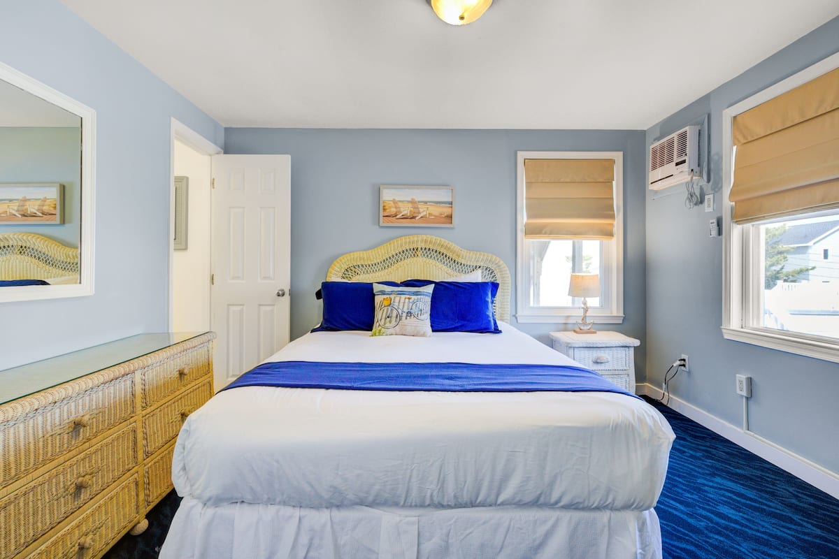 A bedroom with a large bed, a wicker dresser, a nightstand, and two wall-mounted air conditioners.