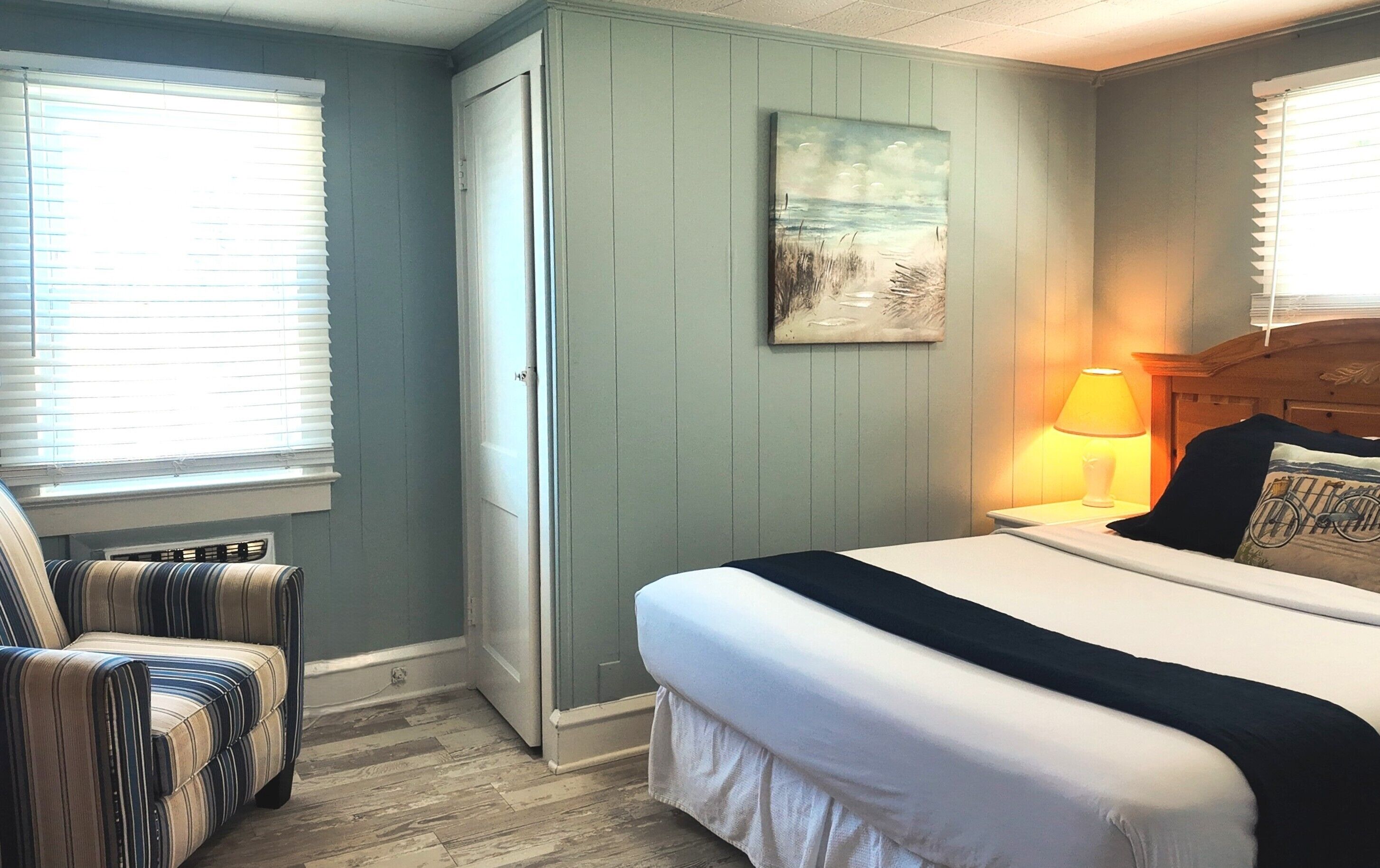 A bedroom with a bed, a chair, a painting, and a lamp.