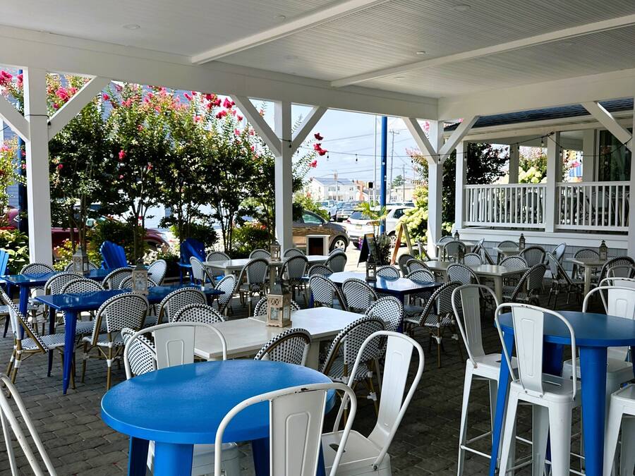 An outdoor café with tables and chairs, a covered area, and a view of the street.
