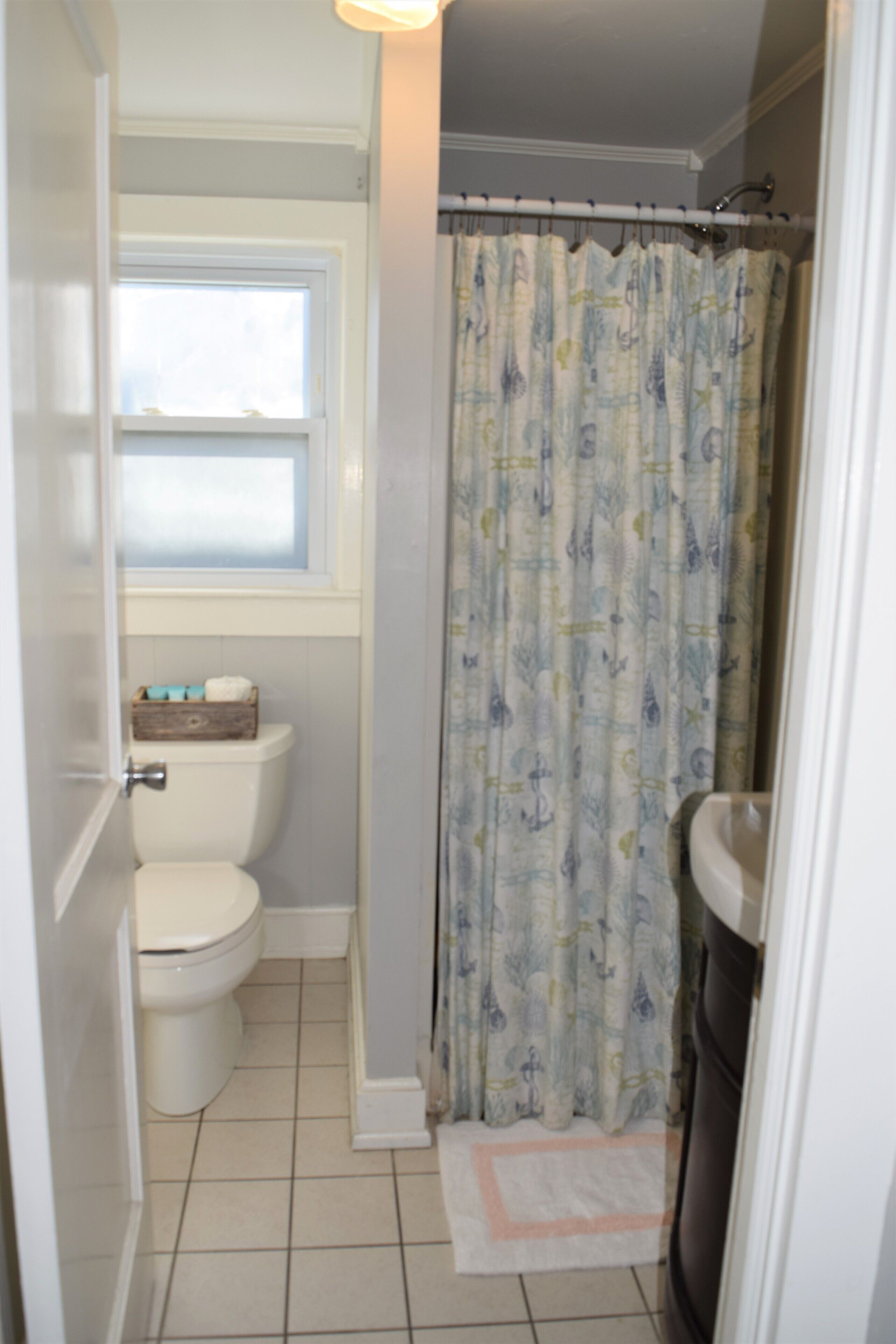 Un baño con inodoro, ventana y cortina de ducha.