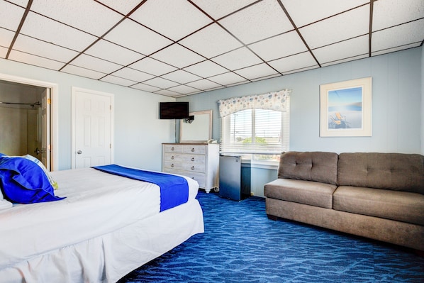 A hotel room with a bed, a dresser, a television, a window with blinds, and a sofa. - Surf City Hotel (Beach Haven)