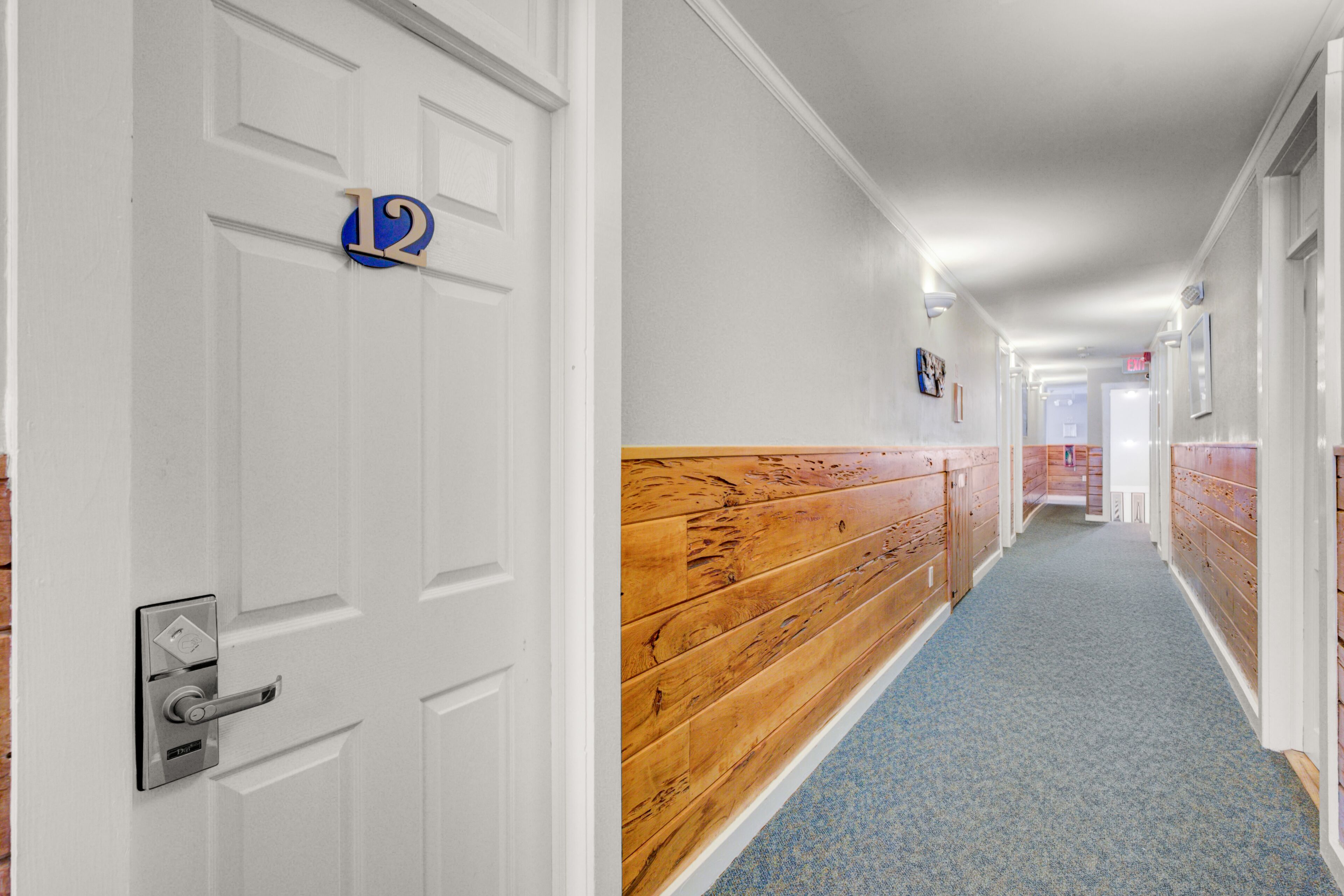 A hallway with a wooden bench, white walls, and a blue carpet.