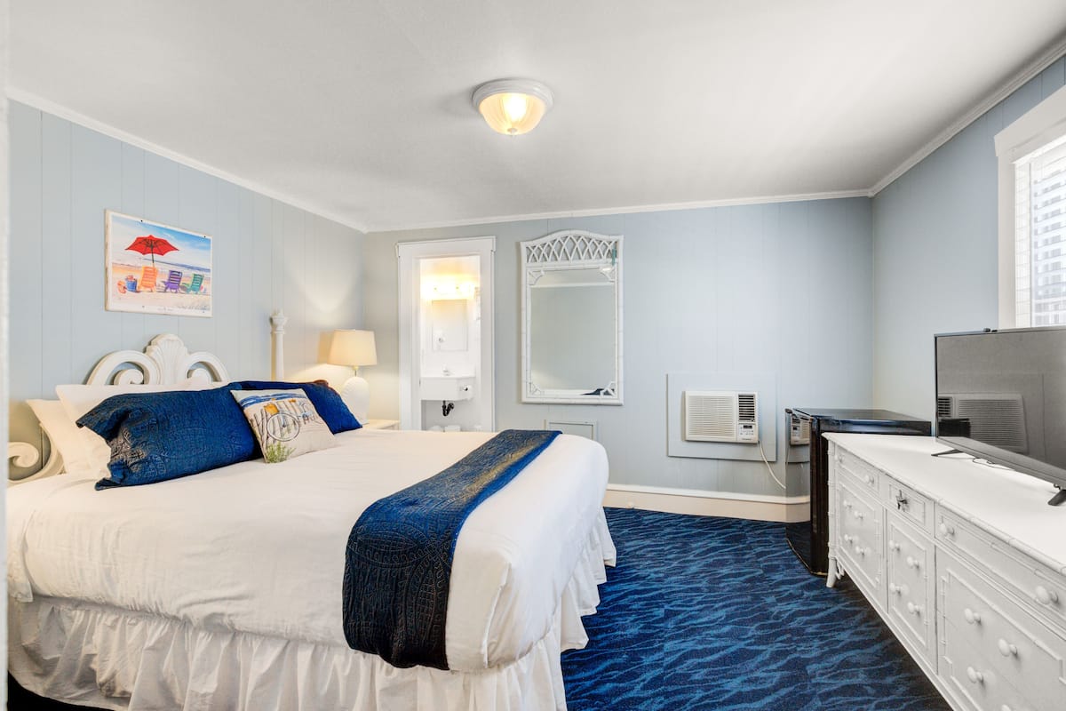A hotel room with a large bed, a dresser, a mirror, a wall-mounted TV, and a window.