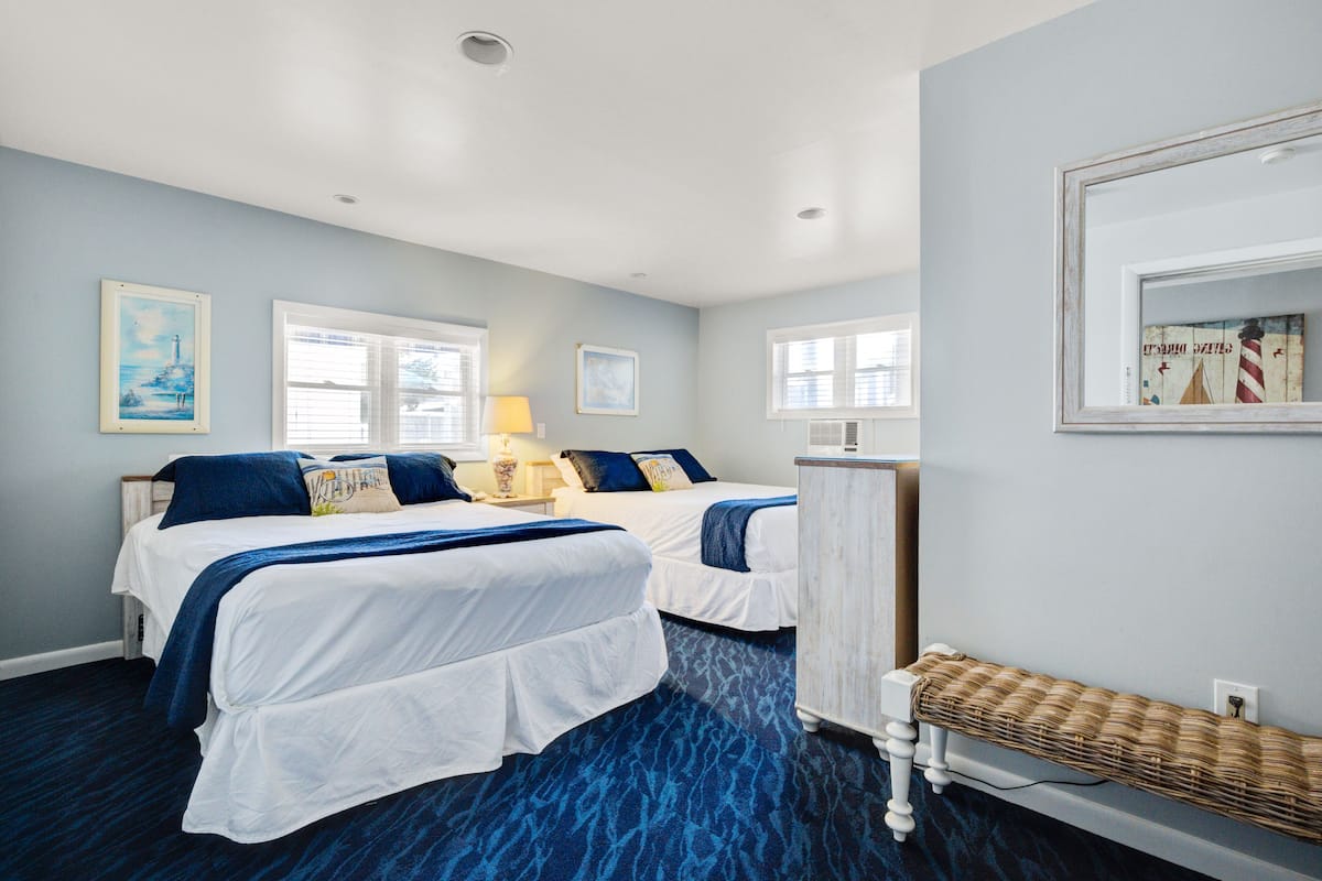 A hotel room with two beds, a small table, and a bench.