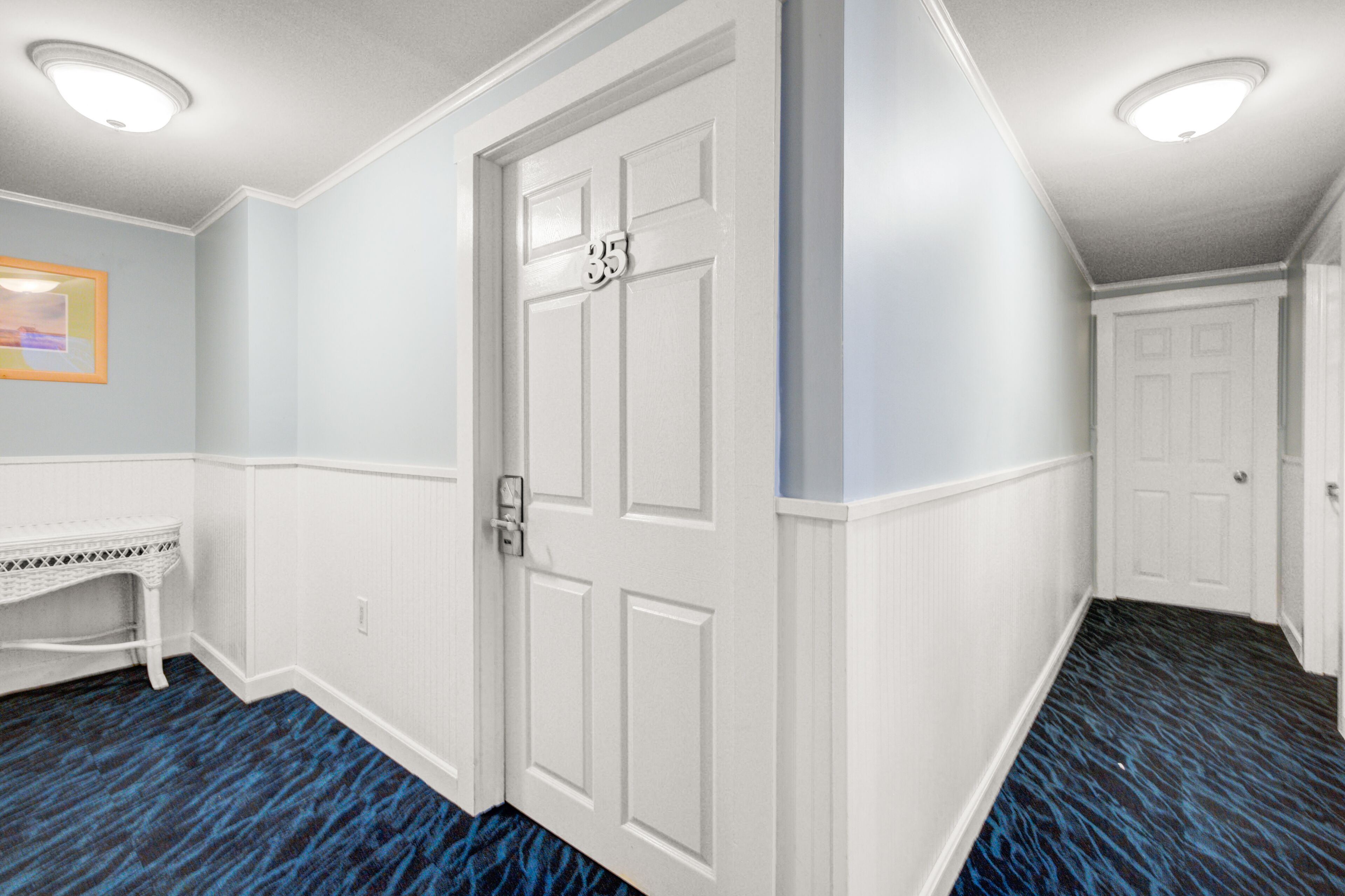 A hallway with a white door marked '35', a white bench, and a patterned blue carpet.
