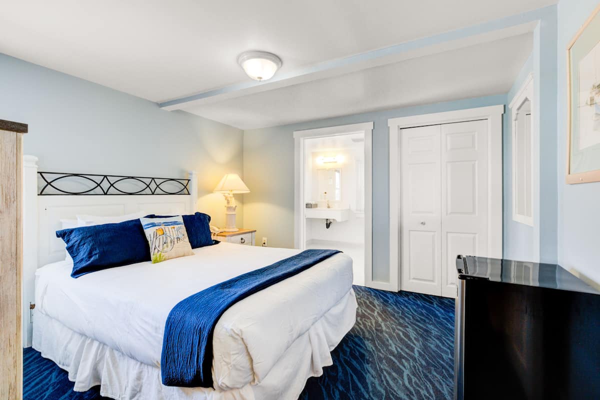 A hotel room with a large bed, a bedside table with a lamp, a wardrobe, and a desk.