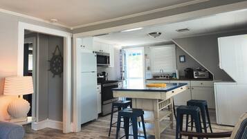 Una cocina compacta con una isla central, taburetes de bar, microondas y un lavamanos.
