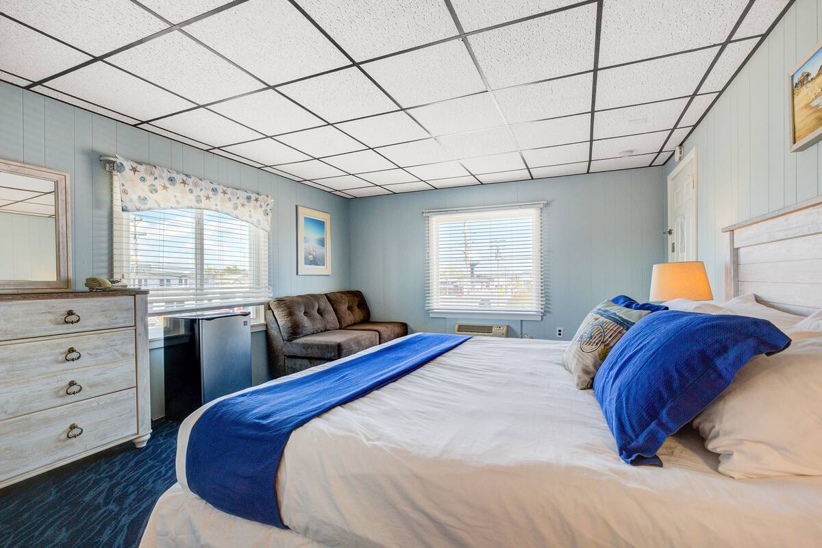 A hotel room with a large bed, a desk, a chair, and a dresser.