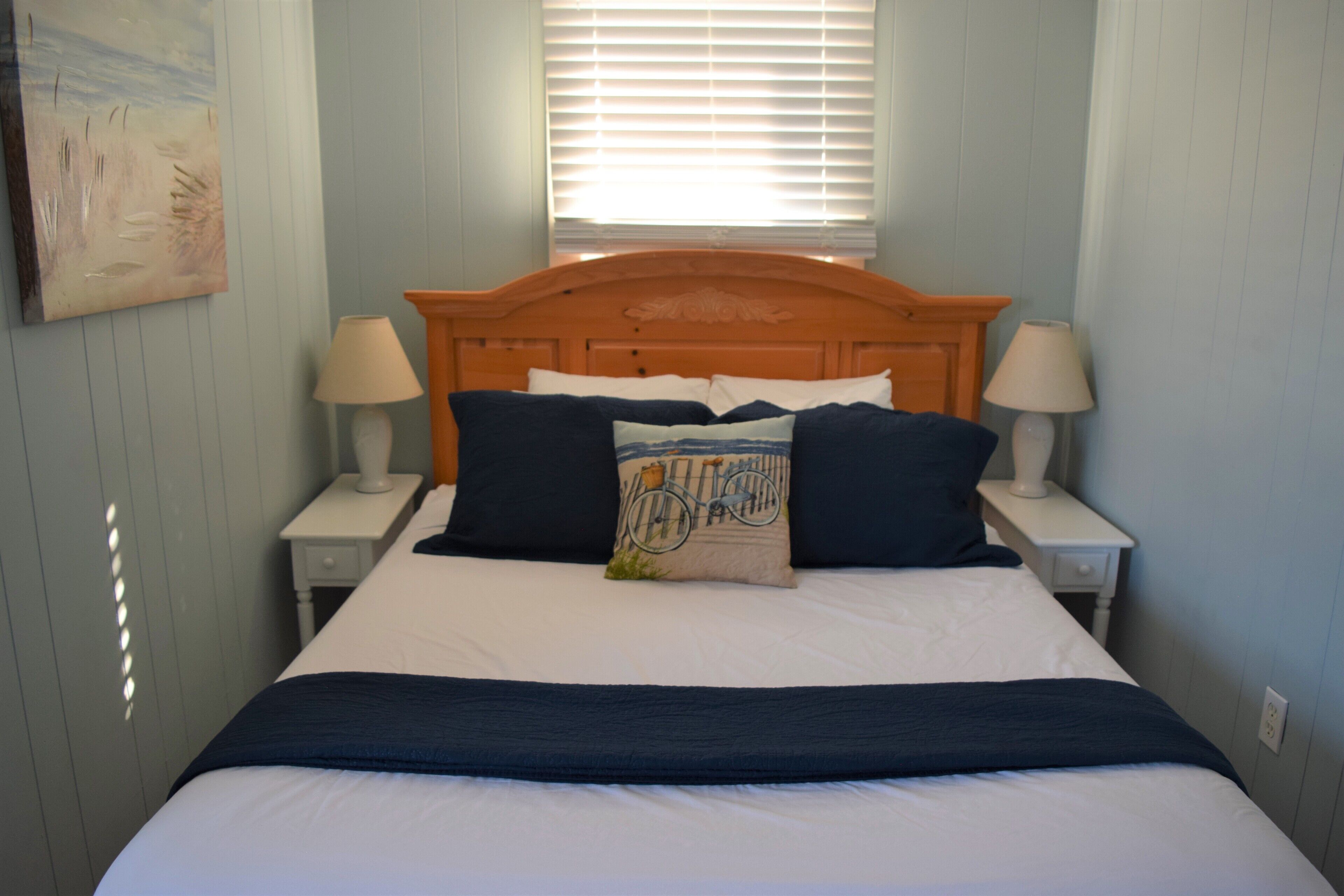 A neatly made bed with a wooden headboard, two bedside lamps, and a window with blinds.