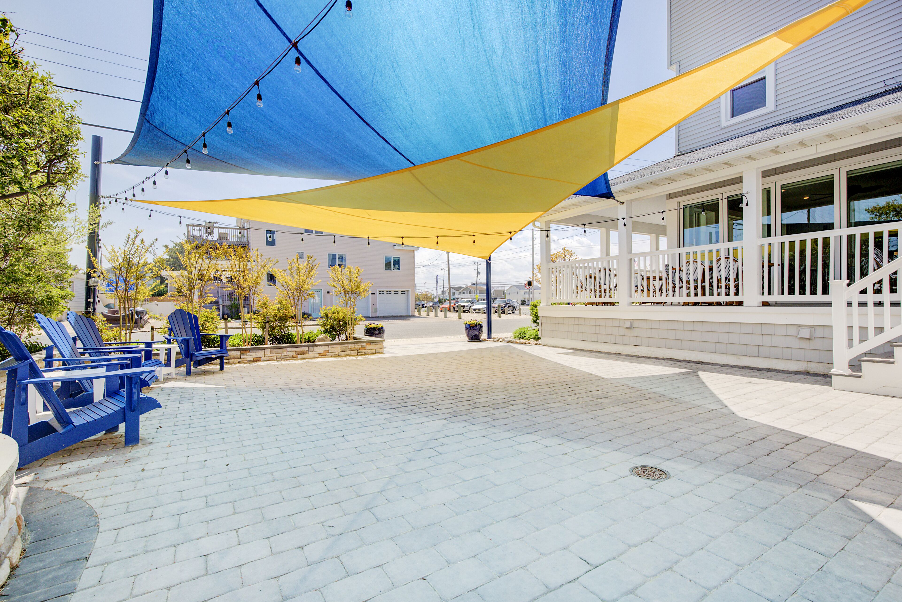 A patio area with blue chairs, a yellow shade sail, and a white building with a balcony.