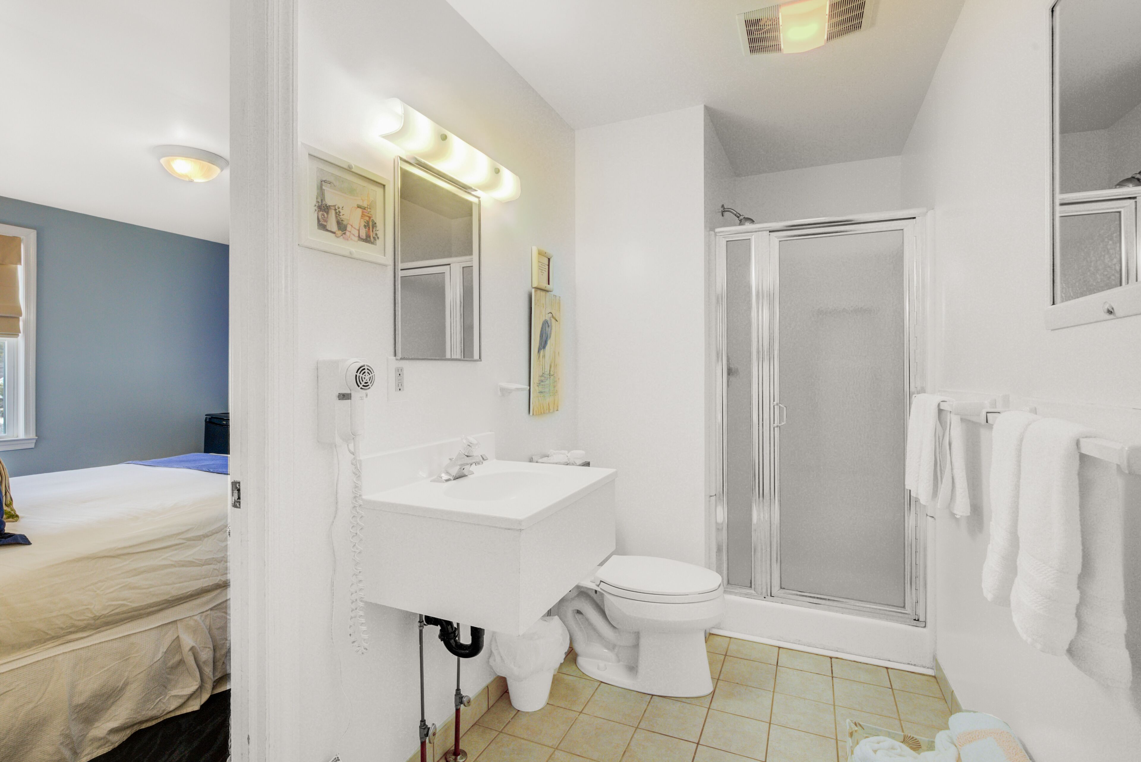 Een badkamer met een witte wastafel, toilet en douche. Er is een spiegel met verlichting erboven en een handdoekrek aan de muur.