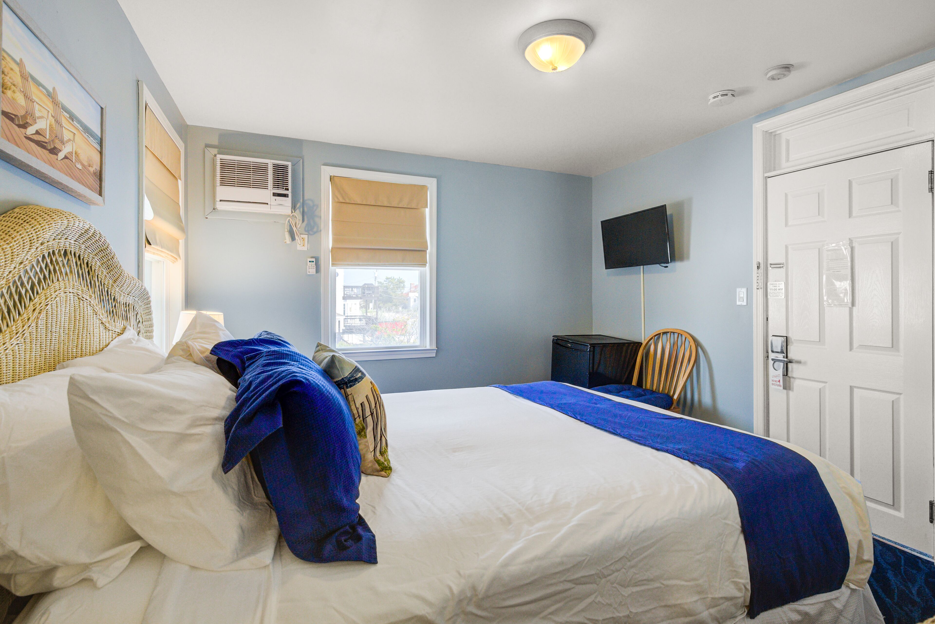 A hotel room with a bed, a television, a window with blinds, and a door.
