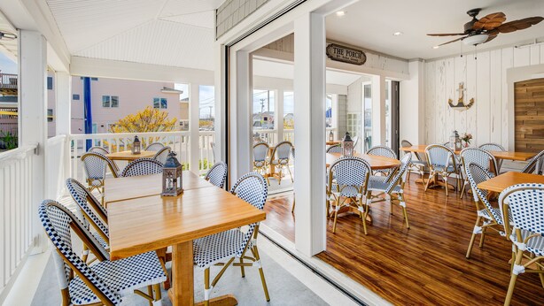 Un restaurante con mesas de madera y sillas con estampado azul y blanco, un ventilador de techo y vistas al exterior.