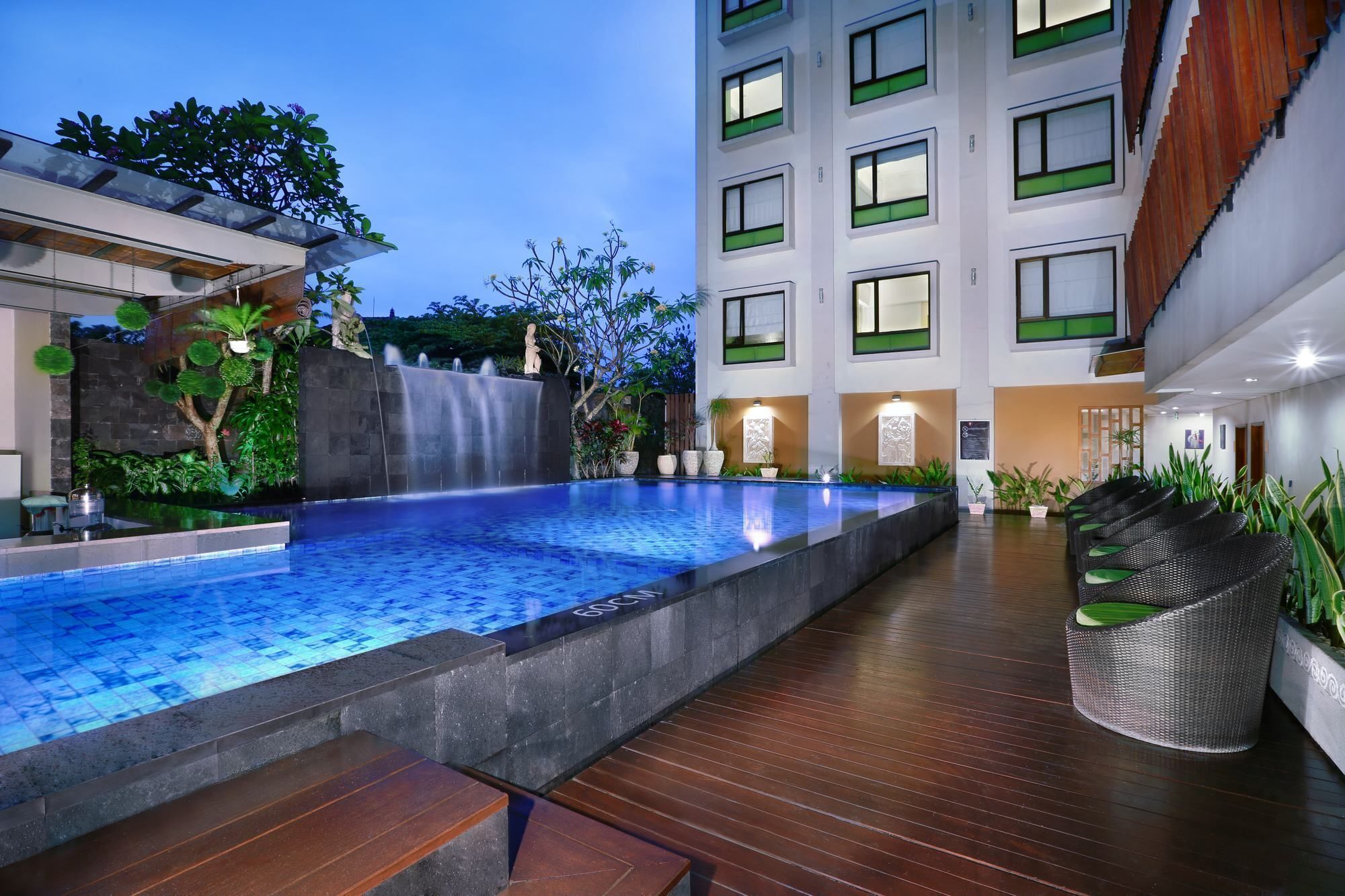A swimming pool with a waterfall feature, surrounded by a wooden deck and potted plants.