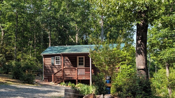A log cabin with a porch, surrounded by trees.