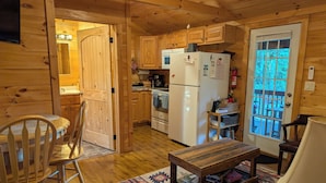 A wooden cabin interior with a dining area, kitchen, and a view through a door.