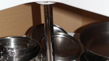 Una encimera de cocina con utensilios de cocina de acero inoxidable, incluyendo ollas y sartenes, y una tetera eléctrica blanca.