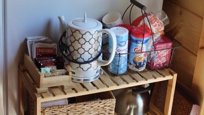 A wooden shelf unit with storage baskets, a coffee maker, and kitchenware.