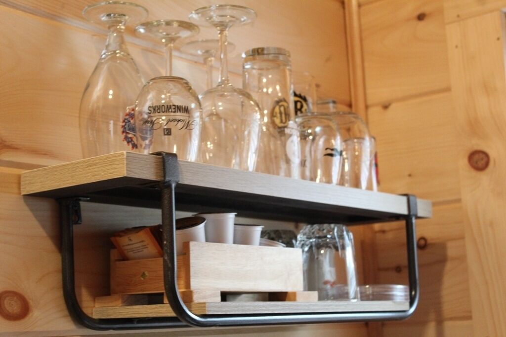 A wooden shelf with wine glasses and jars.