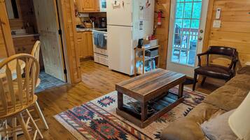 A cozy cabin interior with a wooden dining table, a sofa, and a kitchen area with a refrigerator and wooden cabinets.