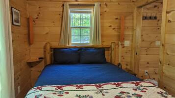 A wooden cabin room with a bed, a window, and a door.