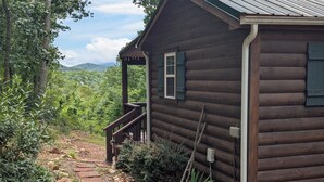 A wooden cabin with a porch, surrounded by a garden path and dense greenery.