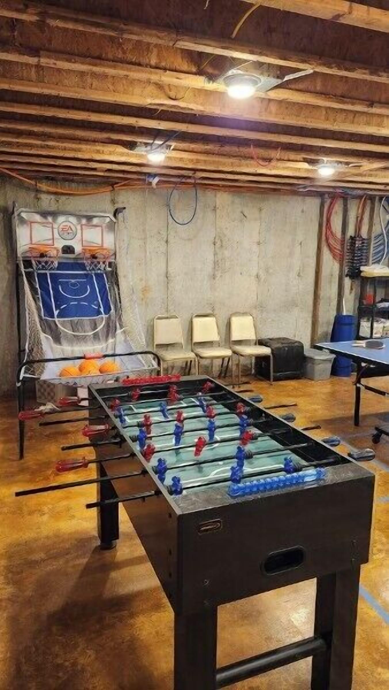 Um quarto com mesa de pebolim, cadeiras e uma cesta de basquete.