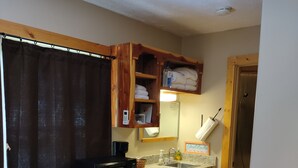 A compact kitchen with wooden cabinets, a microwave, and a sink. - NEW!  Village of Hope - Cabin #1 (Ava)