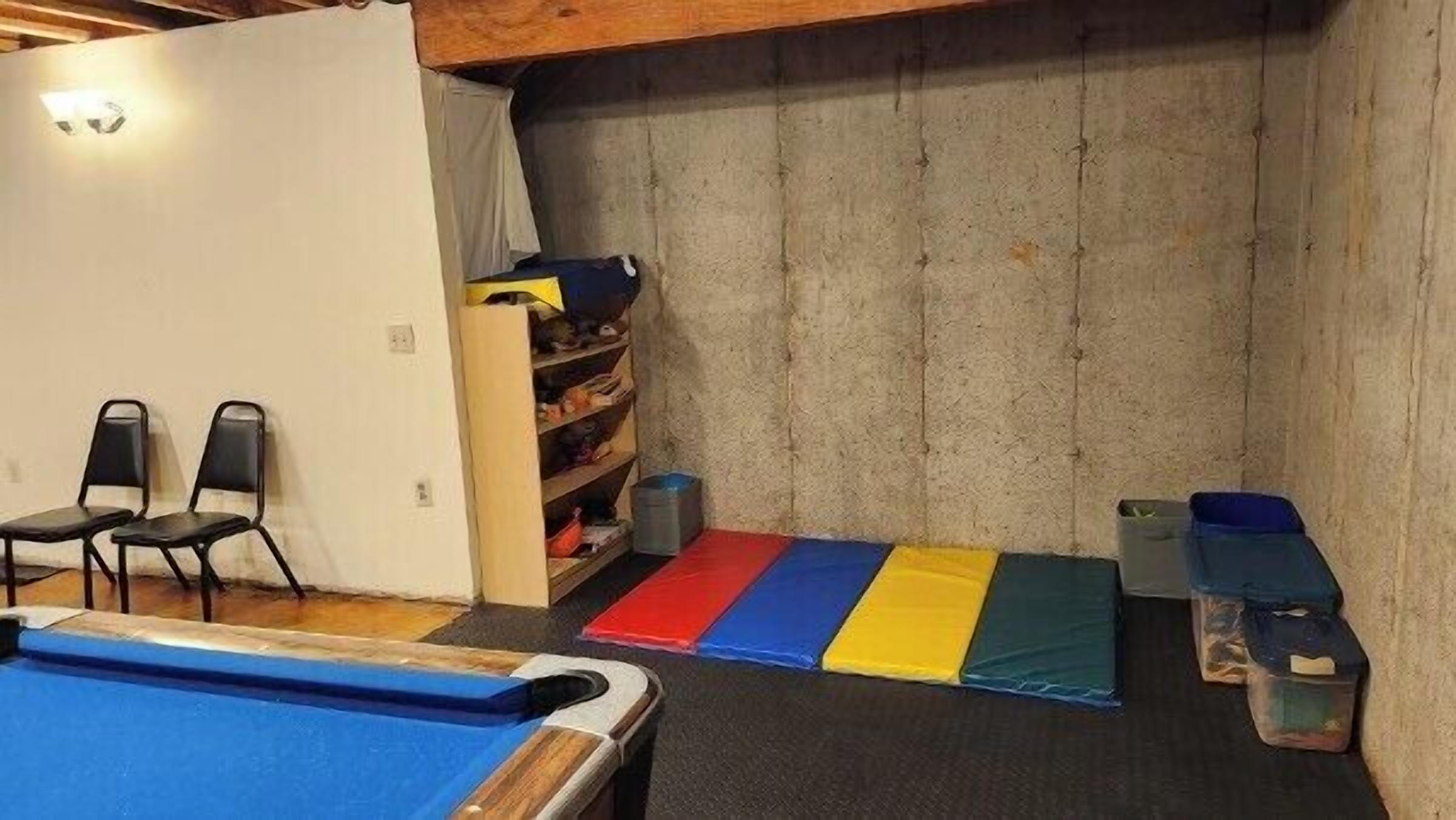 Een kamer met een pooltafel, stoelen, een plank met opbergdozen en een verhoogd, zacht tapijt.