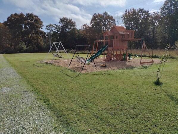 Un parque infantil con una casita de juegos de madera, columpios y toboganes.