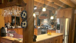 Une cuisine spacieuse dotée de meubles en bois, d’un grand îlot central, d’appareils électroménagers en acier inoxydable et de luminaires suspendus.
