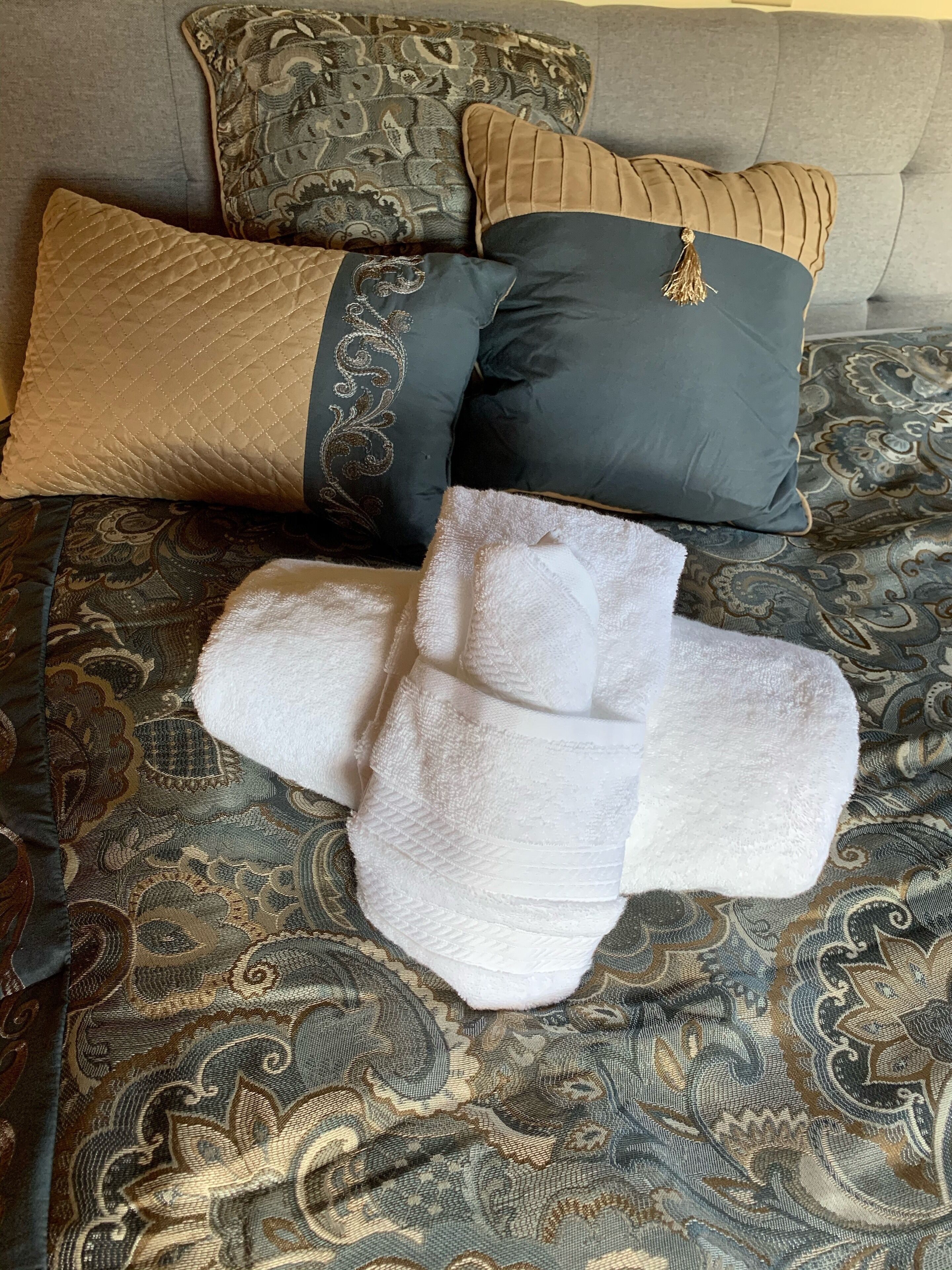 Un lit avec une literie à motifs, deux coussins décoratifs et une serviette blanche pliée.