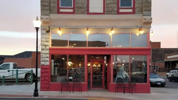 Un bâtiment à deux étages avec une façade rouge et beige, une devanture de magasin dotée de grandes vitrines et un lampadaire devant.