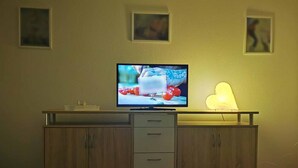 A TV on a wooden cabinet with drawers, a heart-shaped light, and three framed pictures on the wall. - Burgauer Fewo (Burgau)