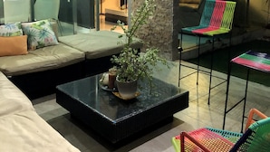 Uma sala de estar moderna com divisória de vidro, um sofá, uma mesa de centro com uma planta e cadeiras coloridas.