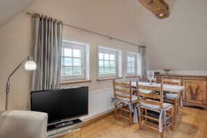 A dining area with a wooden table and chairs, a television, and a window with curtains. - Apartment in historic Spieker on cycling / hiking routes, golf course, forest location close to A 30,  (Bad Bentheim)
