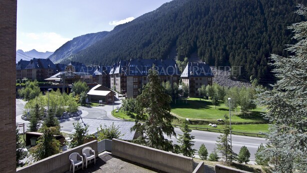 A view of a building with a curved roof, surrounded by trees and a mountain in the background. - Solei - Edificio Bonaigua (Baqueira)