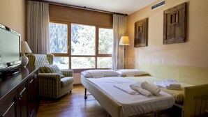 A hotel room with a bed, a chair, a TV, and a window with curtains. - Solei - Edificio Bonaigua (Baqueira)