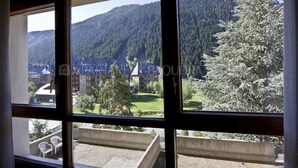 A view from a window overlooking a mountainous area with buildings and trees. - Solei - Edificio Bonaigua (Baqueira)