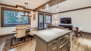 Une cuisine moderne dotée d’un îlot central, de poutres en bois, de grandes fenêtres et d’un coin repas avec un canapé et des fauteuils.
