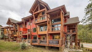 Un chalet en bois à plusieurs étages, doté de balcons et de grandes fenêtres, et entouré d’un paysage naturel.