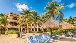 Un resort en la playa con piscina, palmeras y sombrillas de paja.