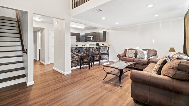 A spacious living room with a brown leather sofa, a wooden coffee table, and a kitchen area with dark cabinets and a tiled backsplash. - 5218 Beach Dr A (Panama City Beach)