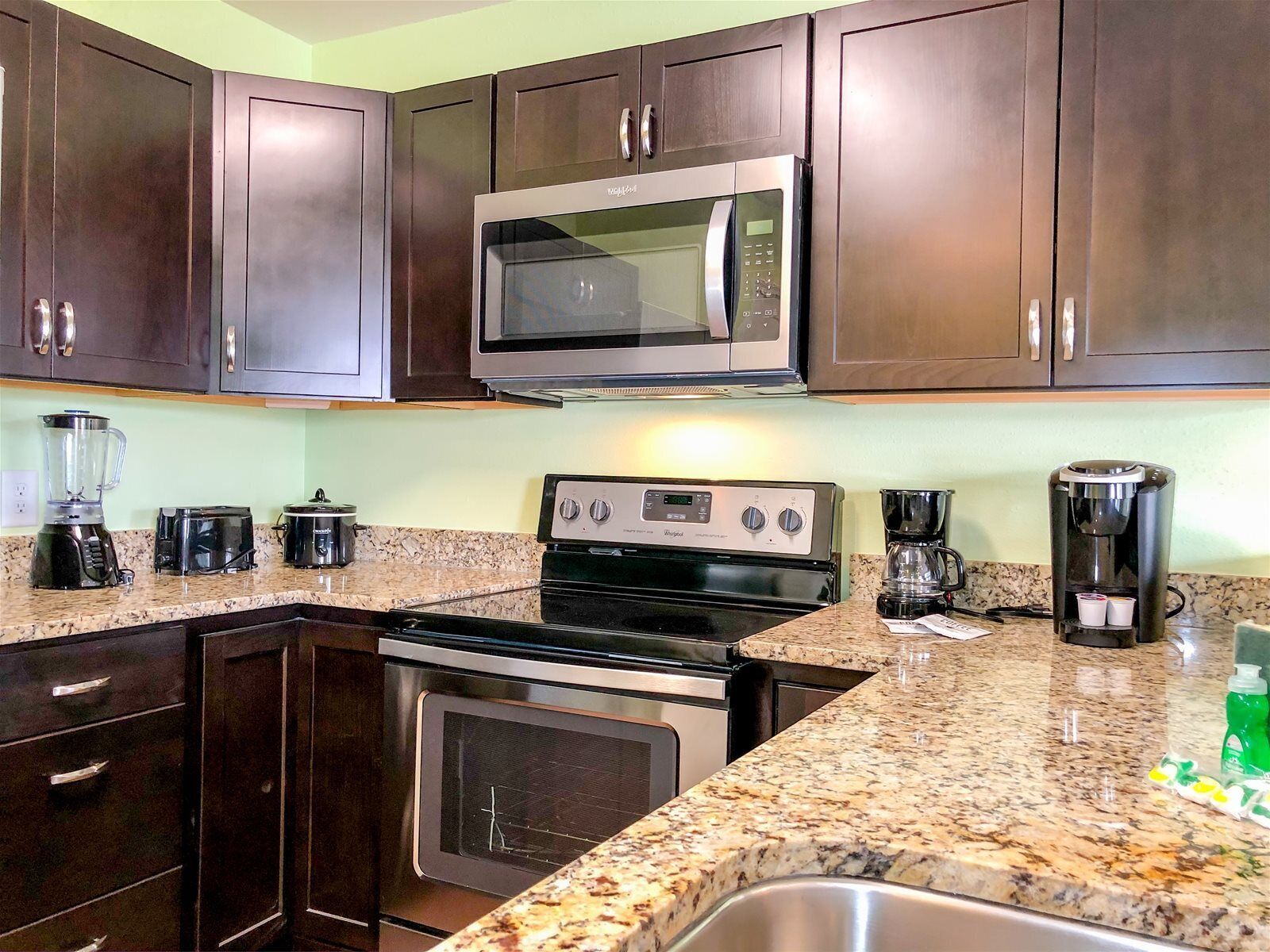A kitchen with dark wooden cabinets, a built-in microwave, a stove, a coffee maker, and a blender.