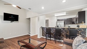 A modern living room with a glass coffee table, a sofa, and a TV mounted on the wall. - 5218 Beach Dr A (Panama City Beach)