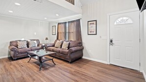 A spacious living room with two leather sofas, a glass coffee table, and a wooden floor. A white door and a window with curtains are visible. - 5218 Beach Dr A (Panama City Beach)