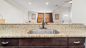 A kitchen with granite countertops, a stainless steel sink, and dark wooden cabinets. - 5218 Beach Dr A (Panama City Beach)