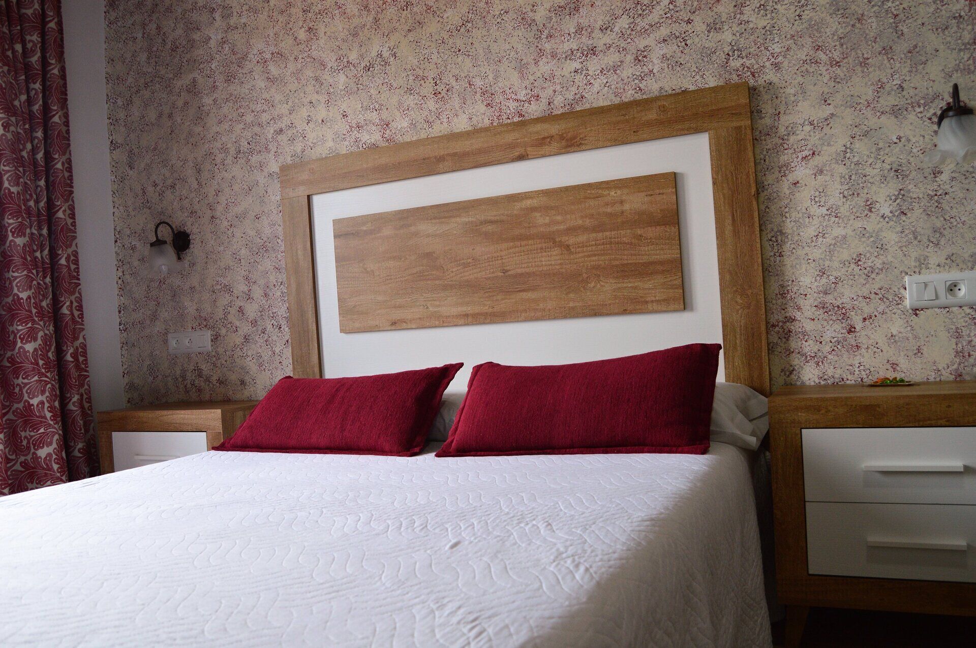 A bed with a wooden headboard, two red pillows, and a white quilted bedspread.